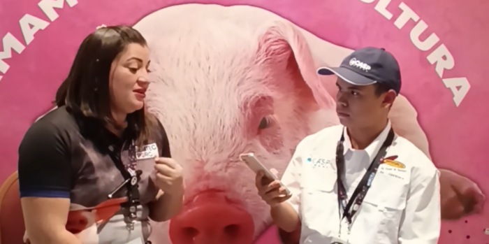 Entrevista a mujer joven de contextura gruesa por un joven usando un teléfono, en un seminario de porcicultura.